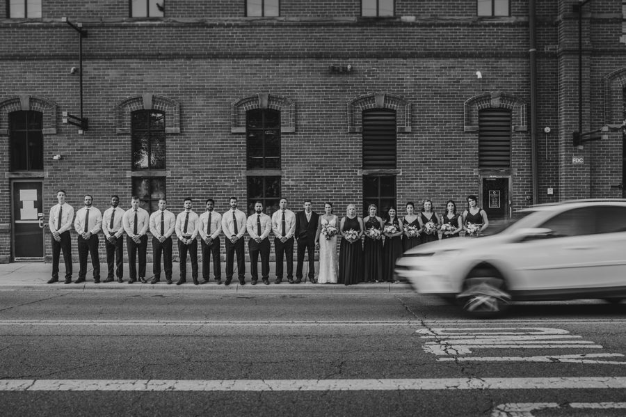 black and white photo of wedding party with car driving by