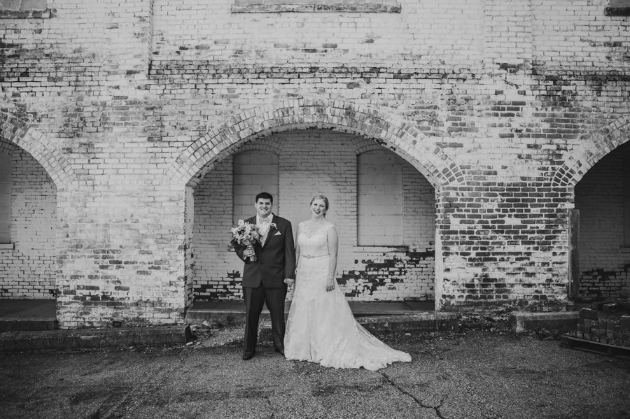 black and white photo of bride and groom holding hands on white washed brick wall