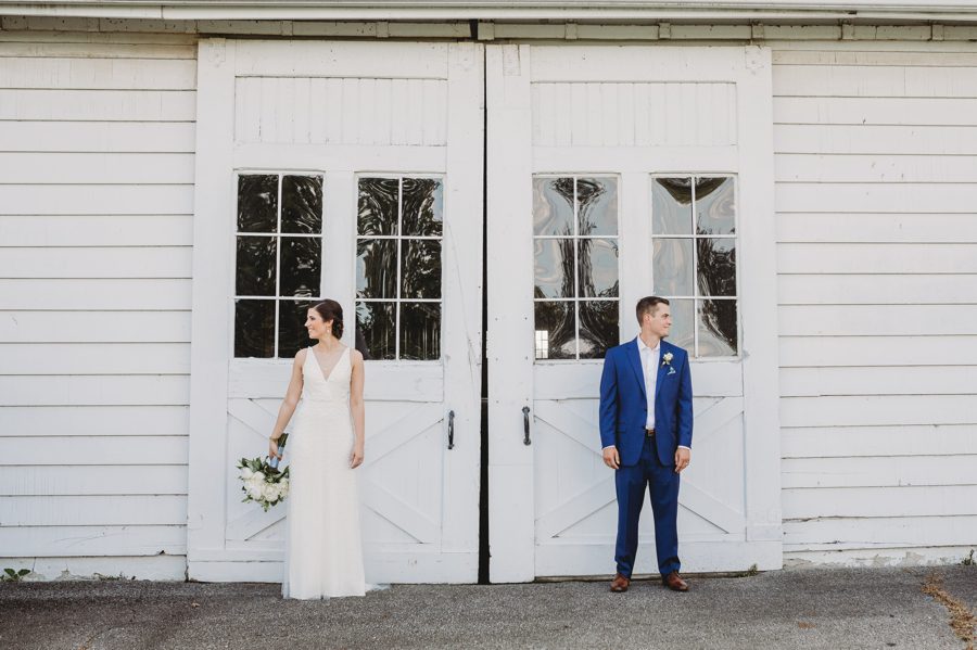 Wide angle of Kelsey and Jon looking away from each other while in front of white barn