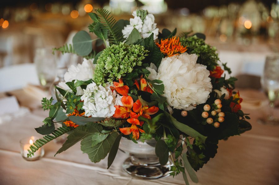 Orange and white centerpiece with lush greenery for reception
