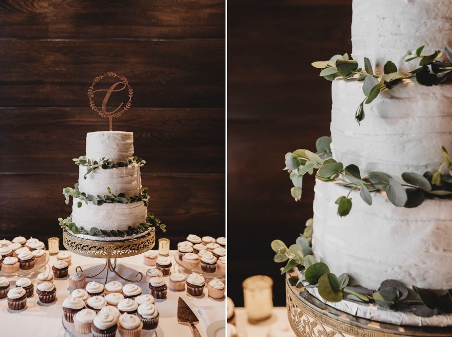 White wedding cake decorated with eucalyptus in front of wood wall