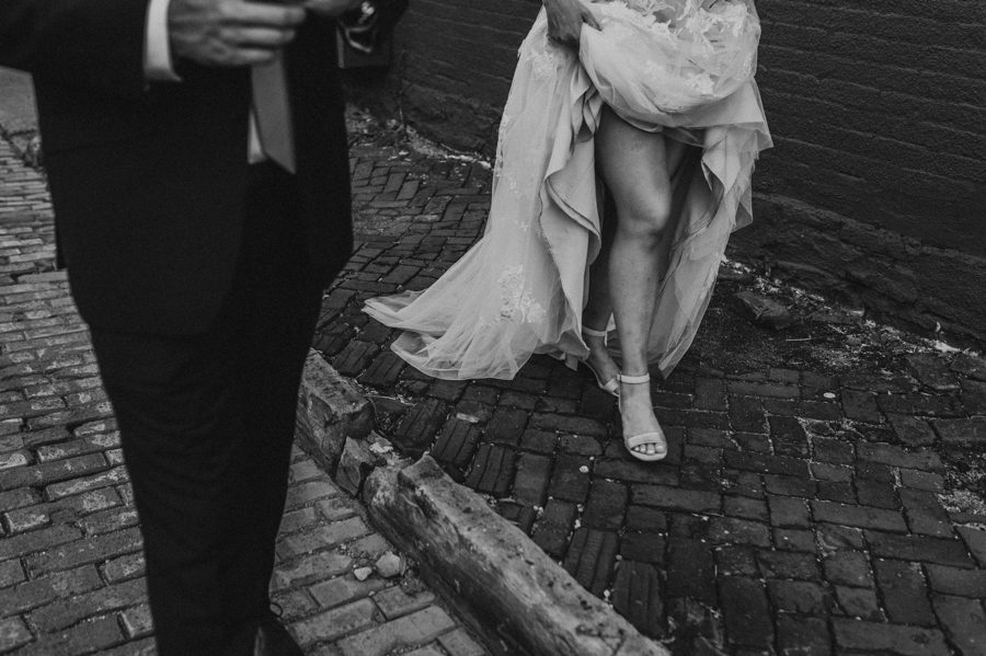 Black and white capture of Emilee walking and holding up wedding gown