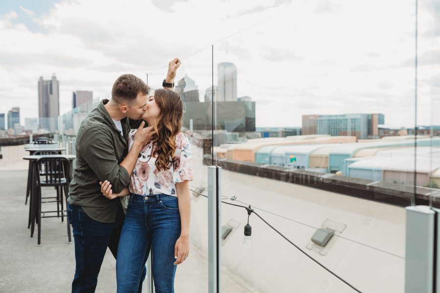 man kissing fiancé at glass-enclosed rooftop bar in Columbus Ohio