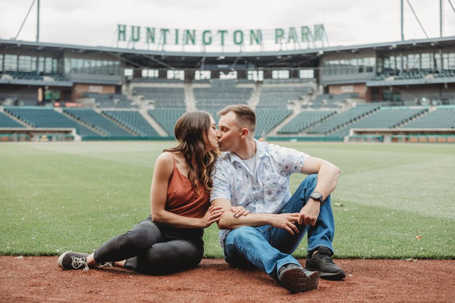 Huntington Park Engagement Photos of engaged couple kissing while sitting on baseball diamond