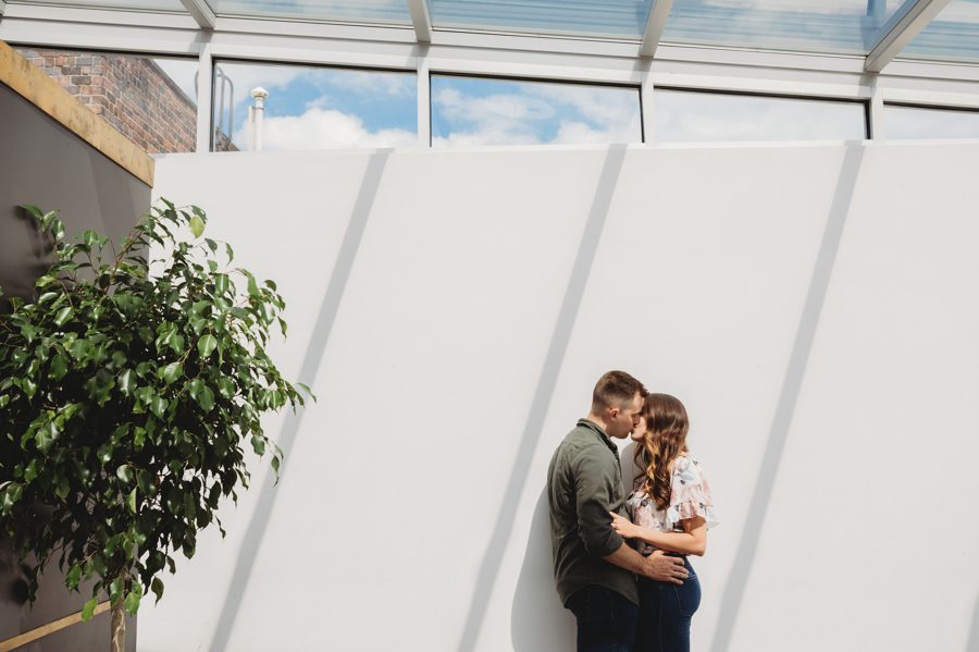 engaged couple kissing on white wall with shadows of sunlight