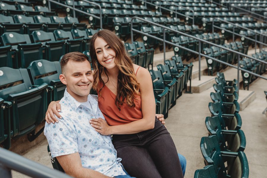woman sitting on fiancés lap in stadium seats at Huntington Park Engagement Photos