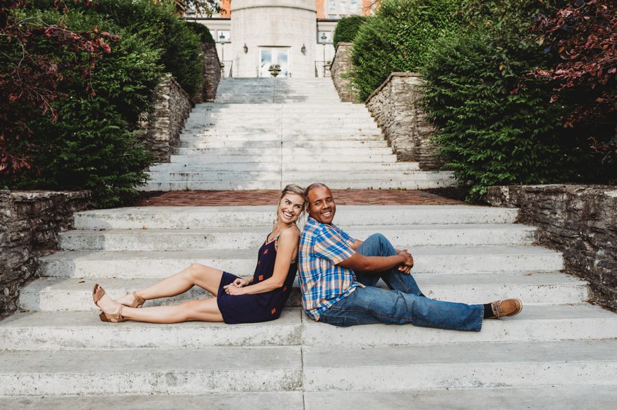 Engaged interracial couple sitting on steps back to back to each other smiling