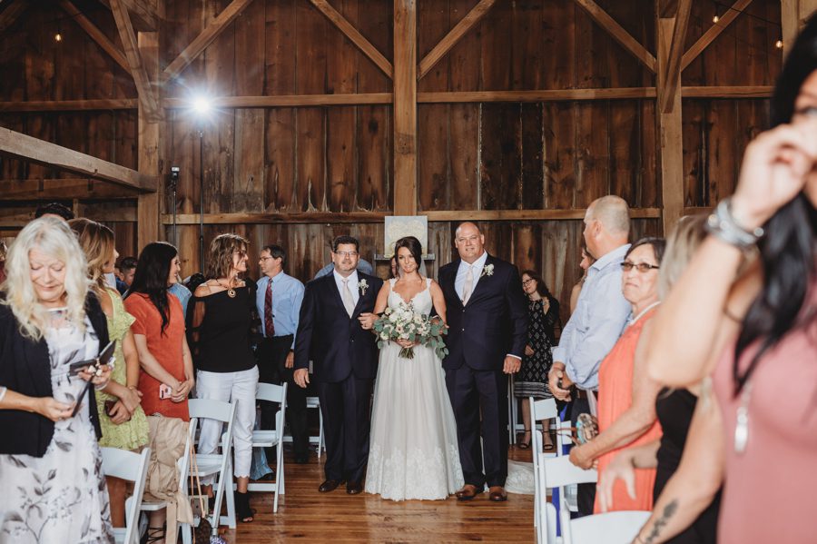 Cortni being escorted down the aisle by her father and step father at Rusty River Barn